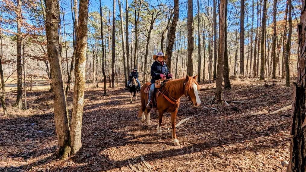 Two visitors enjoy a horseback ride on the trails of Oakfuskee Conservation Center.