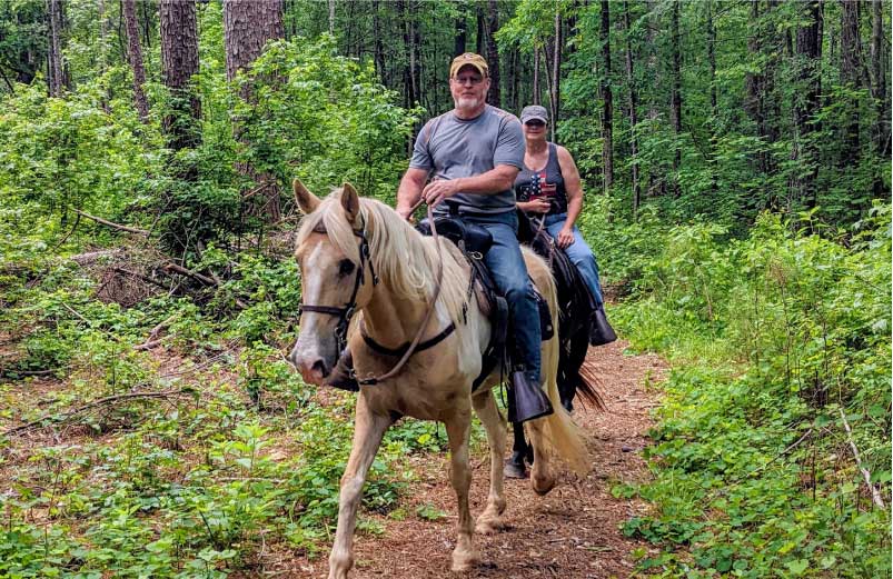 Two visitors to Oakfuskee Conservation Center enjoy a trail ride on horseback.